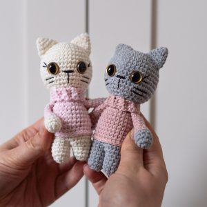 Dwie szydełkowe maskotki kotki w różowych sweterkach trzymane w dłoniach