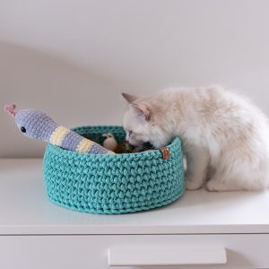 Koszyk na zabawki dla kota miętowy do którego zagląda puchaty kot. z koszyka wystaje pluszowy wąż z kocimiętką.